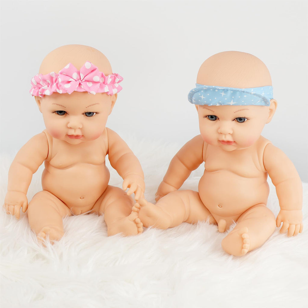 Two anatomically correct 14-inch twin dolls, one with a pink polka dot headband and the other with a blue star-patterned headband, sitting on a fluffy white surface. They have soft facial features and are designed for imaginative play. Perfect for children who love dolls. BiBi Dolls.